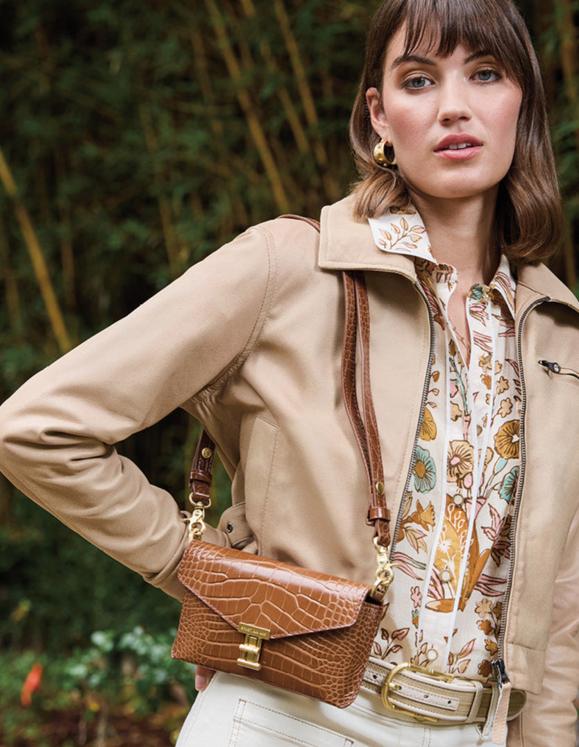 Woman wearing a beige coat and holding a brown handbag in a forest setting