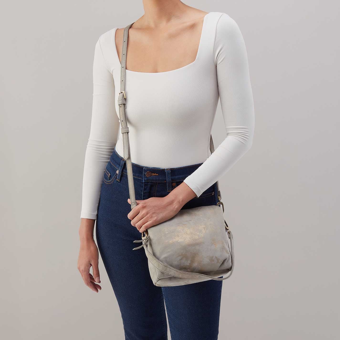 Person wearing a white long-sleeve top and blue jeans, holding a gray leather bag against a plain background