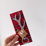Decorative antler-shaped bottle opener on a red plaid card held by a hand against a white background