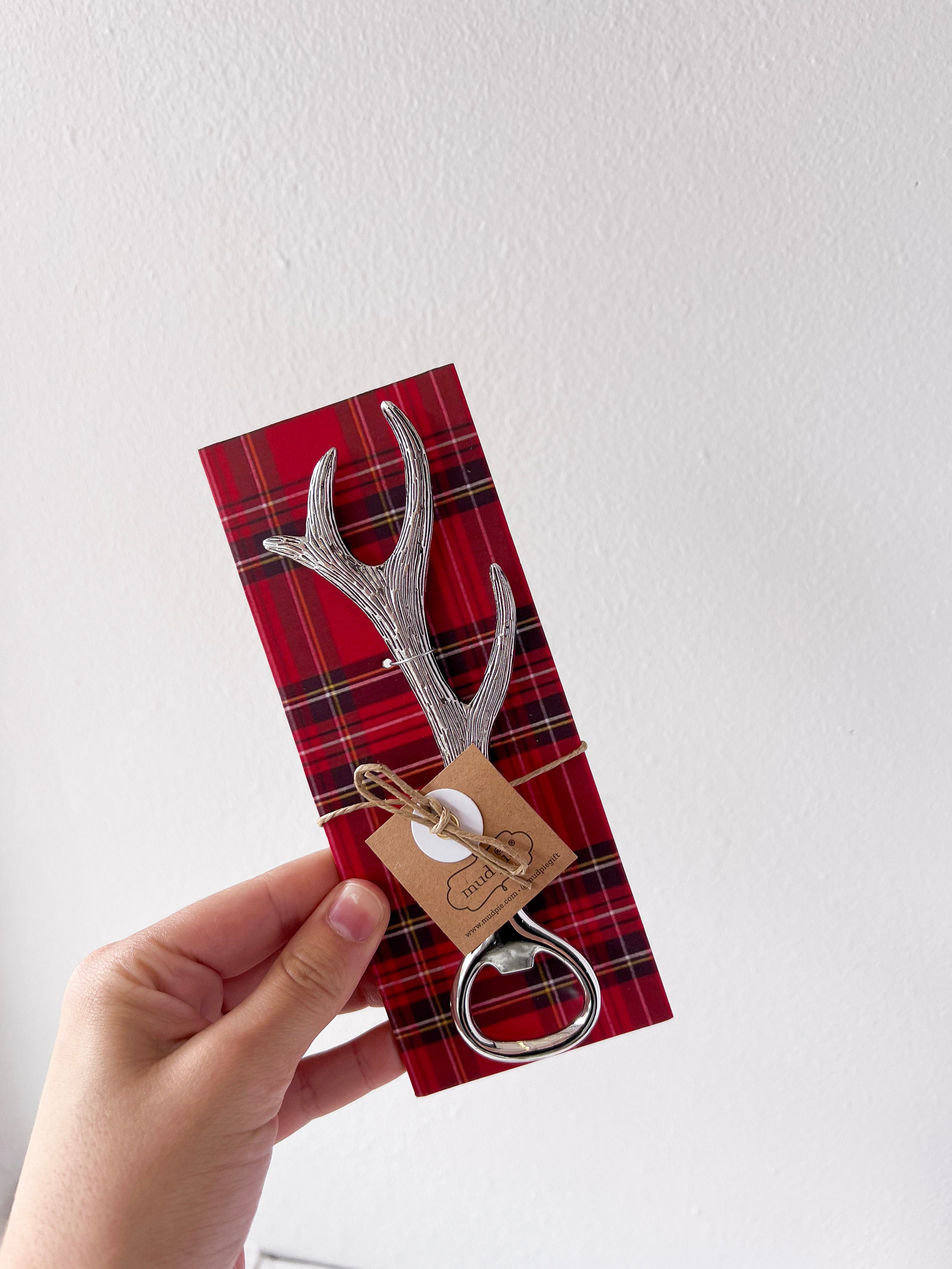 Decorative antler-shaped bottle opener on a red plaid card held by a hand against a white background