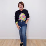 Person wearing a black sweater with a colorful design and blue jeans on a plain white background