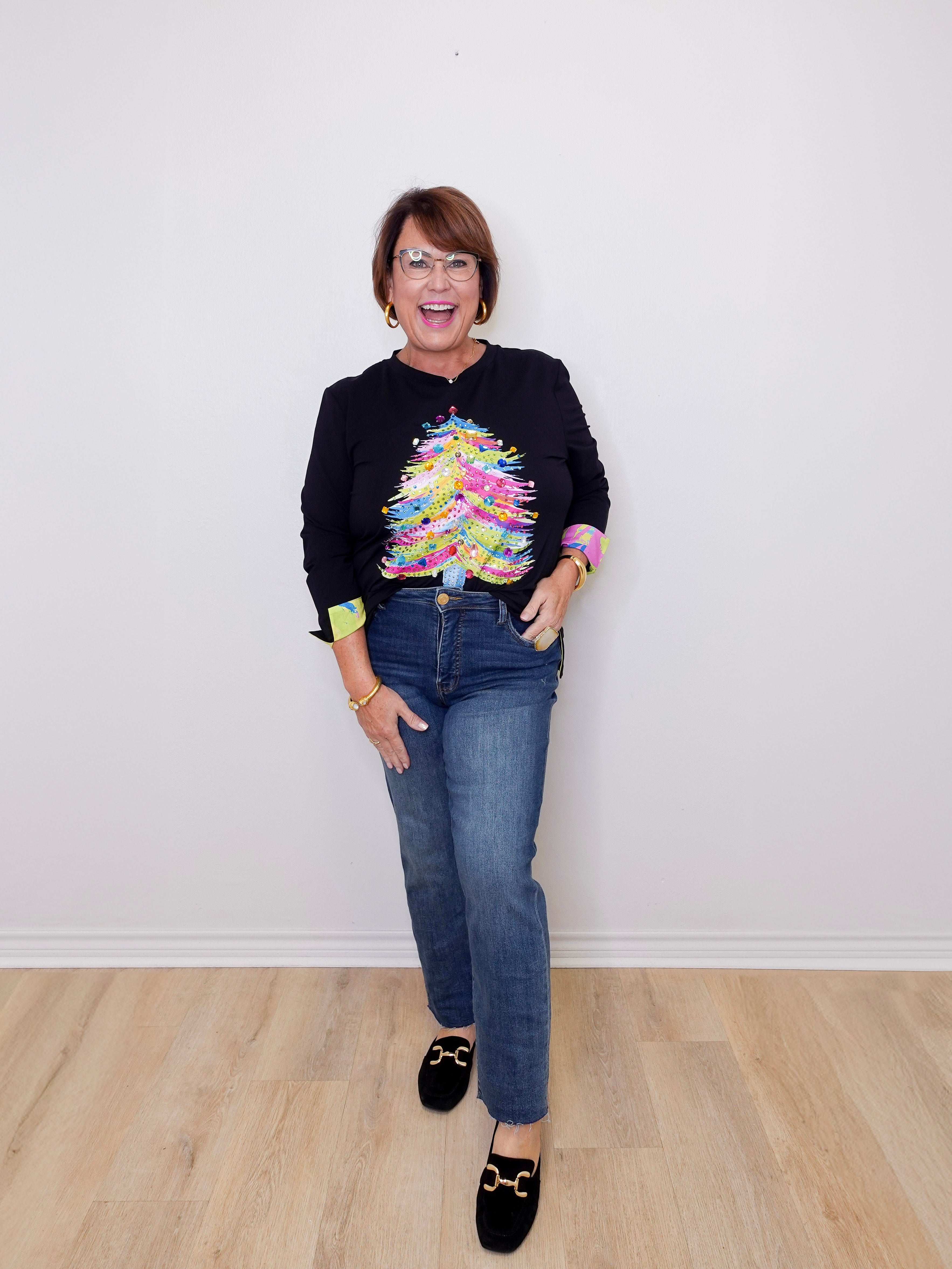Person wearing a black sweater with a colorful design and blue jeans on a plain white background