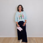 Woman wearing a light blue sweatshirt with a graphic design, dark pants, and white sneakers, holding a pink clutch.