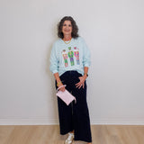 Woman wearing a light blue sweatshirt with a graphic design, dark pants, and white sneakers, holding a pink clutch.