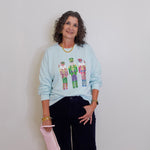 Woman wearing a light blue sweatshirt with colorful designs, standing against a plain white wall.