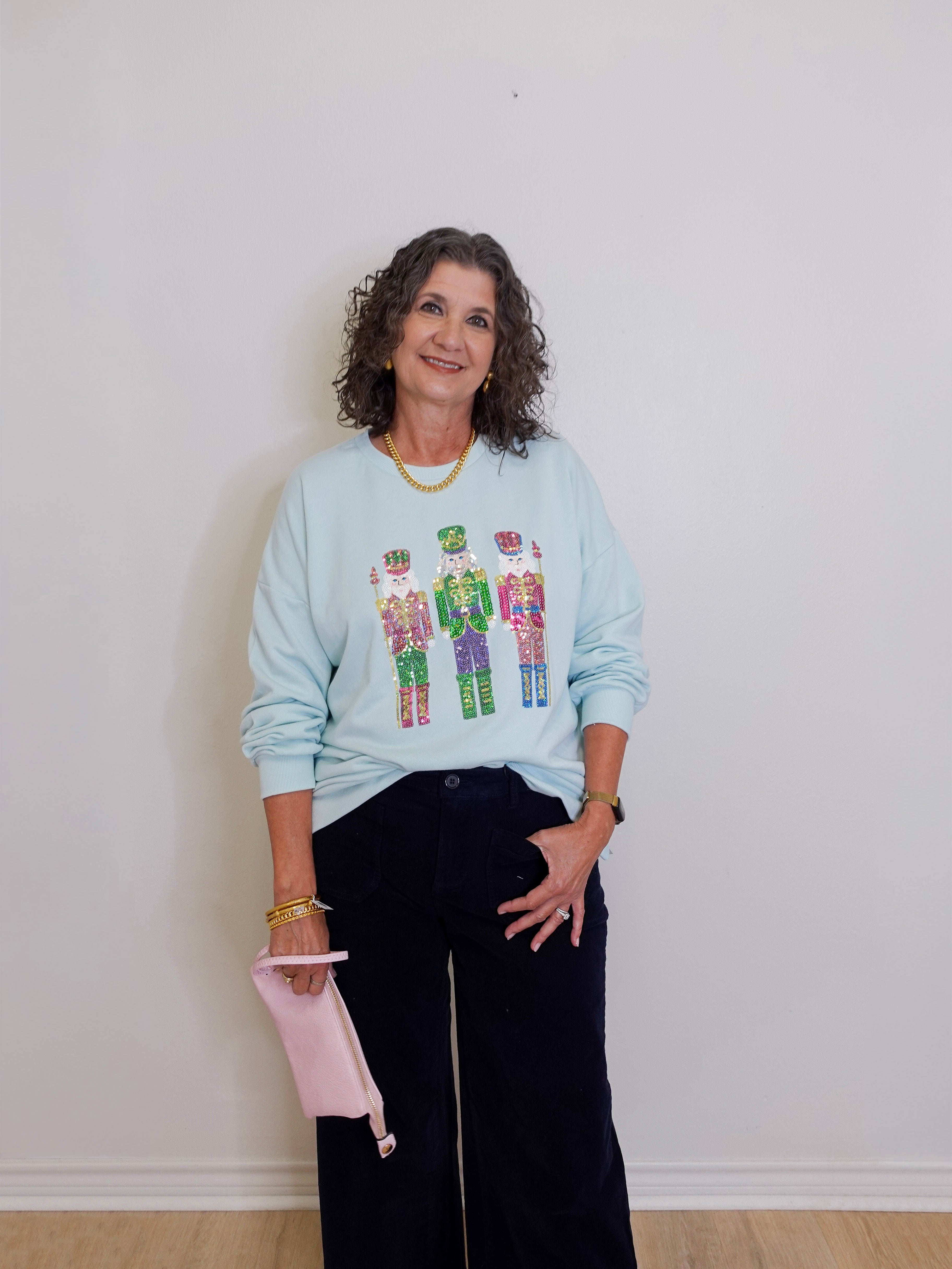 Woman wearing a light blue sweatshirt with colorful designs, standing against a plain white wall.