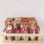 Set of candy scoops with Christmas-themed toppers in a wooden crate on a white background
