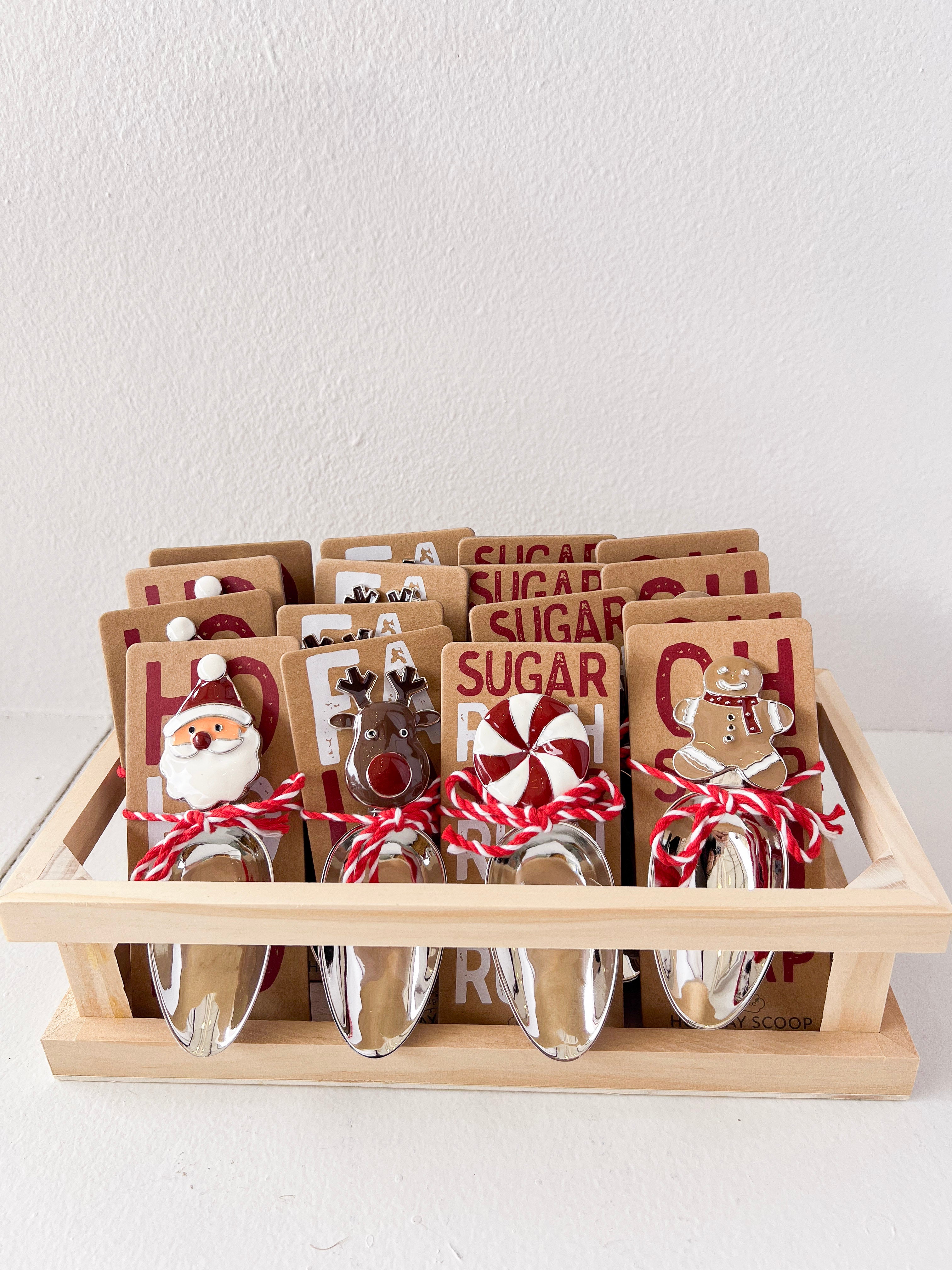 Set of candy scoops with Christmas-themed toppers in a wooden crate on a white background