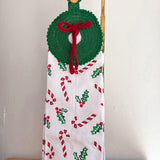 Decorative towel with Christmas patterns and a green wreath holder on a stand.
