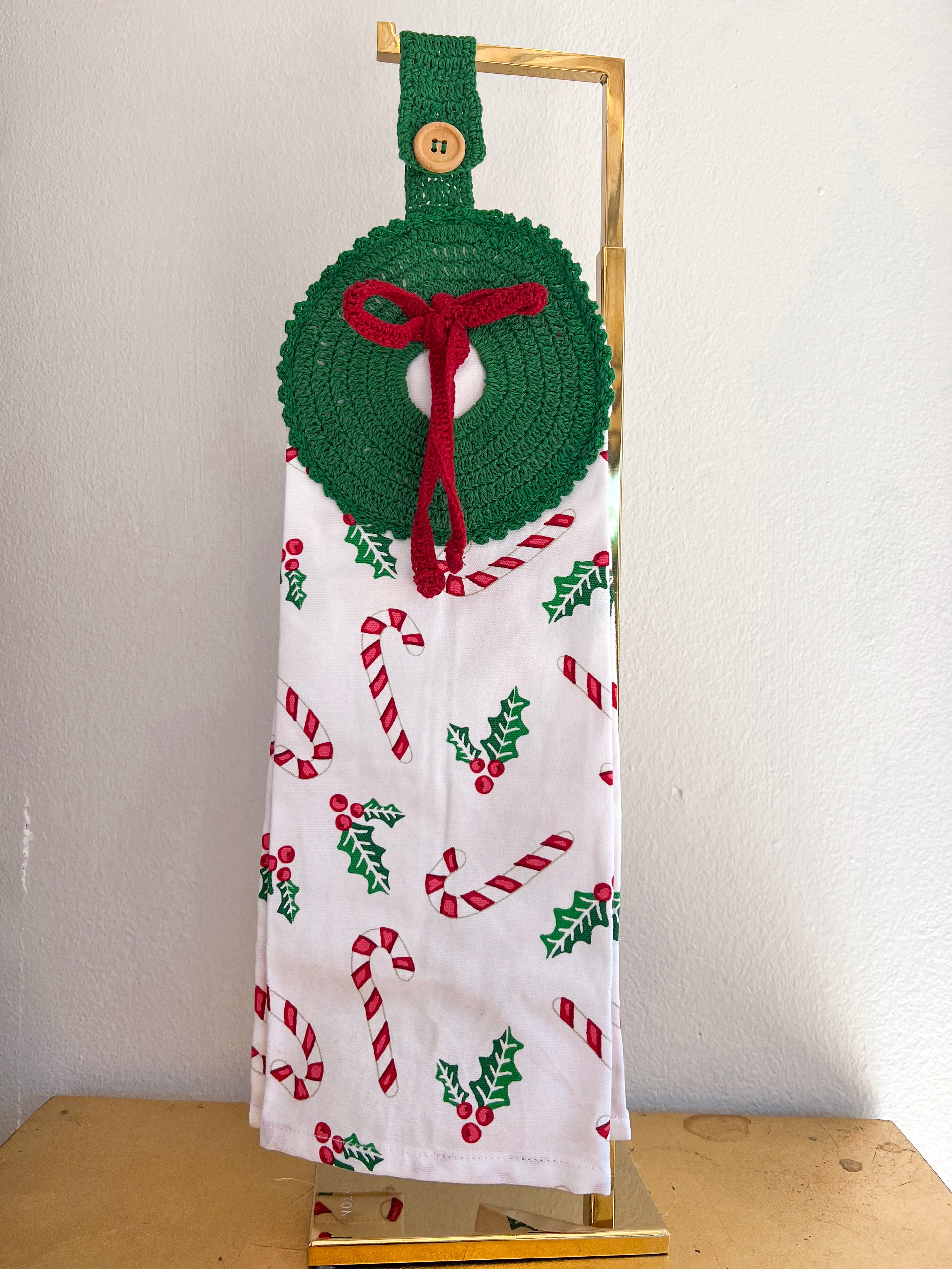 Decorative towel with Christmas patterns and a green wreath holder on a stand.