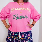 Person wearing a pink sweatshirt with 'Champagne & Mistletoe' text and patterned shorts.