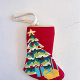 Red Christmas-themed needlepoint stocking with a tree and presents design on a white background
