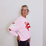 Person wearing a pink sweatshirt with red text and graphics against a white background