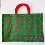 Green fabric bag with red bow pattern and red handle on a white background