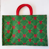 Green fabric bag with red bow pattern and red handle on a white background