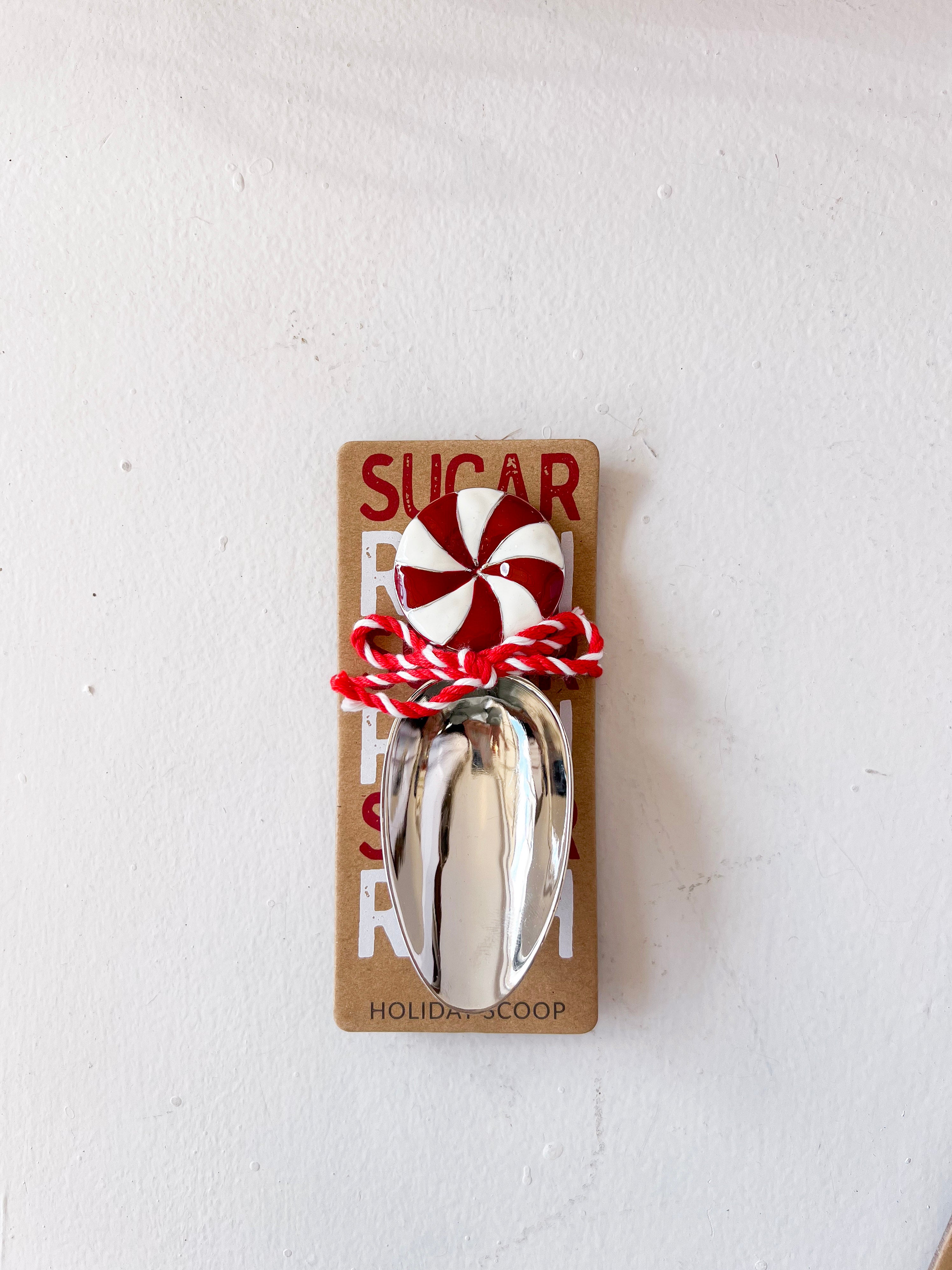 Metallic sugar scoop with peppermint candy on a cardboard holder against a white background