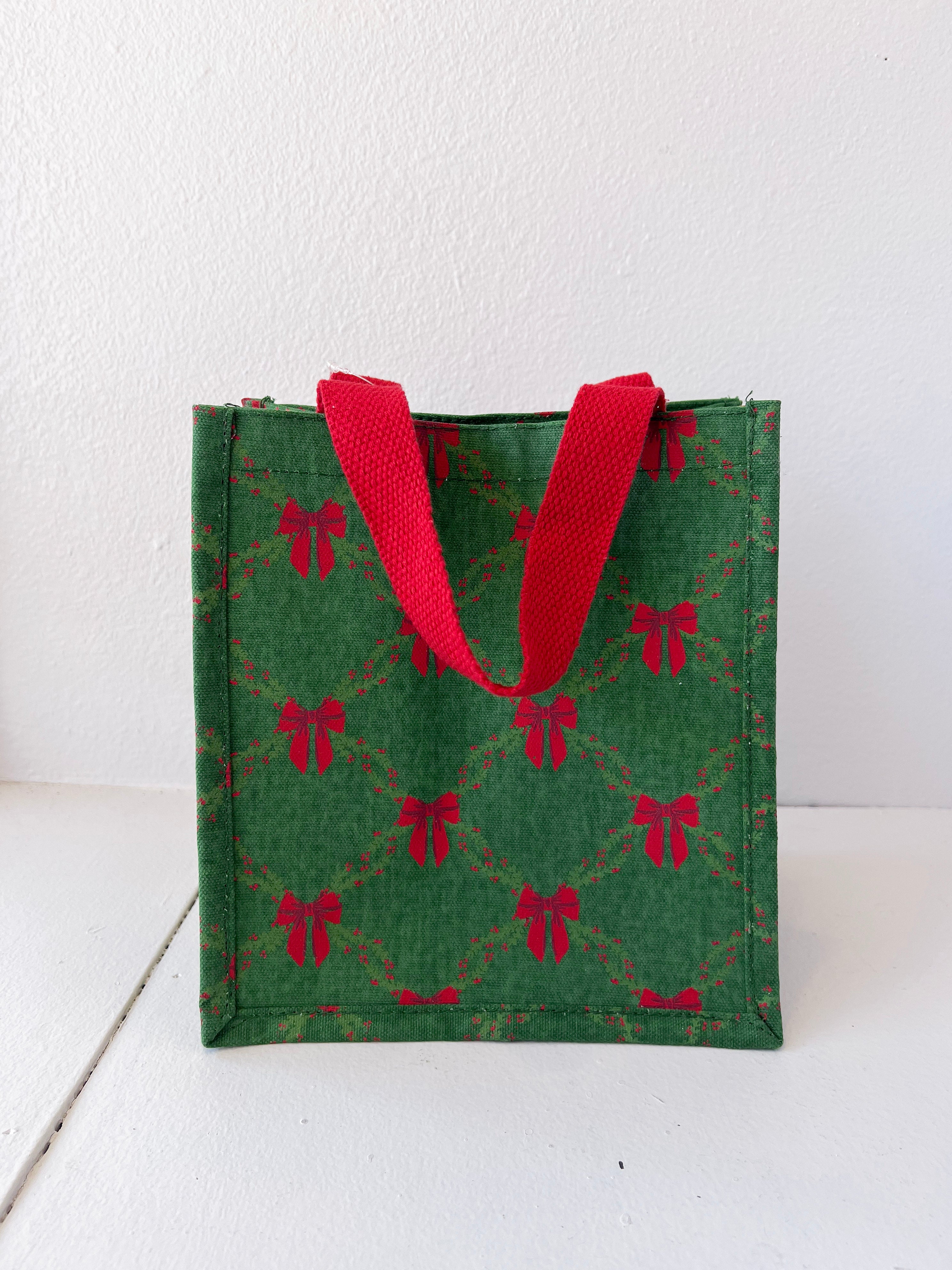 Green gift bag with red bow pattern and red handles on a white background