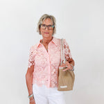 Woman wearing a pink floral blouse and white pants, holding a beige handbag against a white background