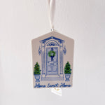 Decorative hanging ornament with blue door and wreath design on a white background