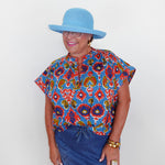 Woman wearing a colorful patterned shirt and blue hat against a white background