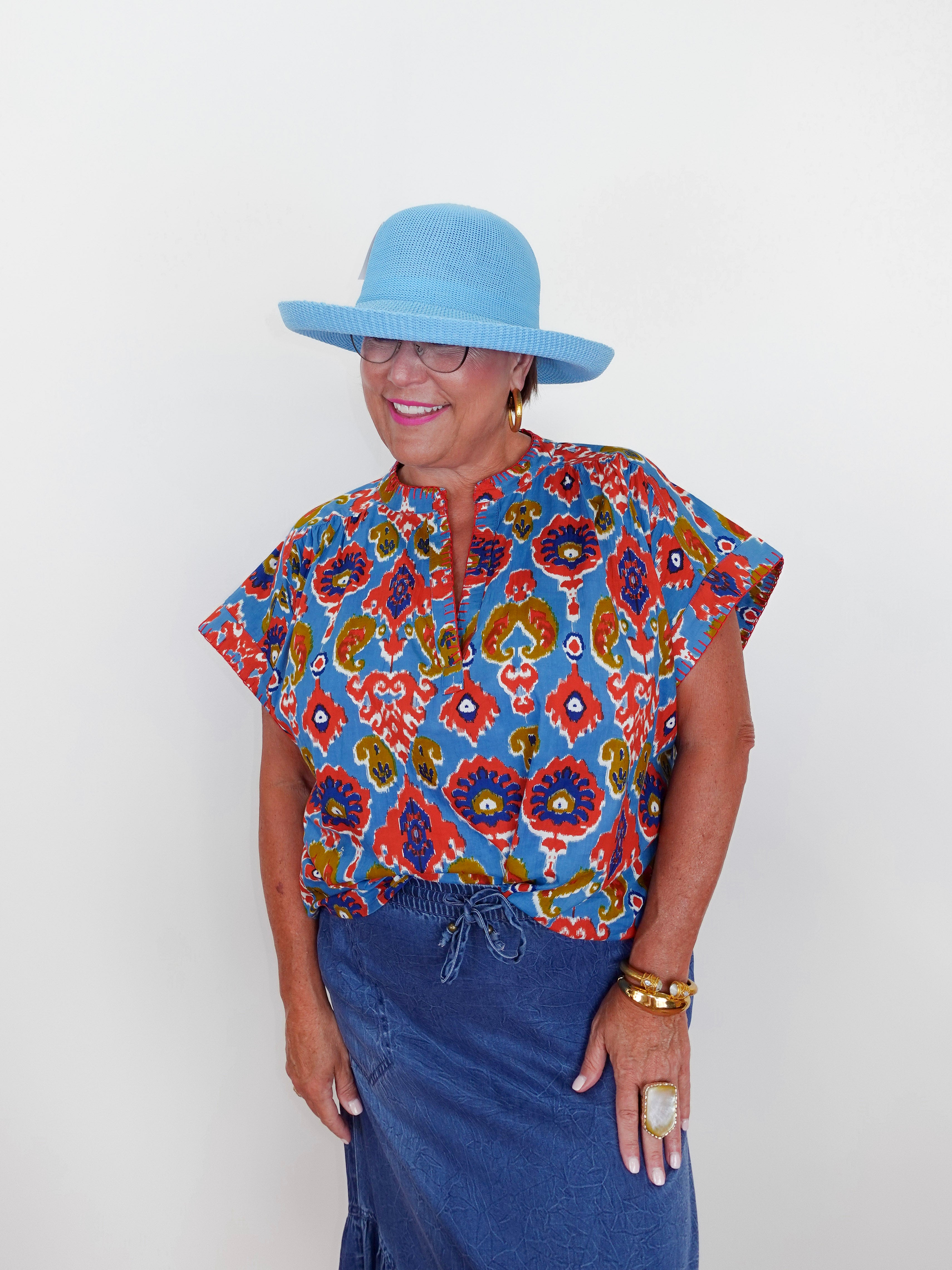Woman wearing a colorful patterned shirt and blue hat against a white background