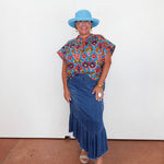 Woman wearing a colorful top and blue skirt with a blue hat against a white background