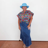 Woman wearing a colorful top and blue skirt with a blue hat against a white background
