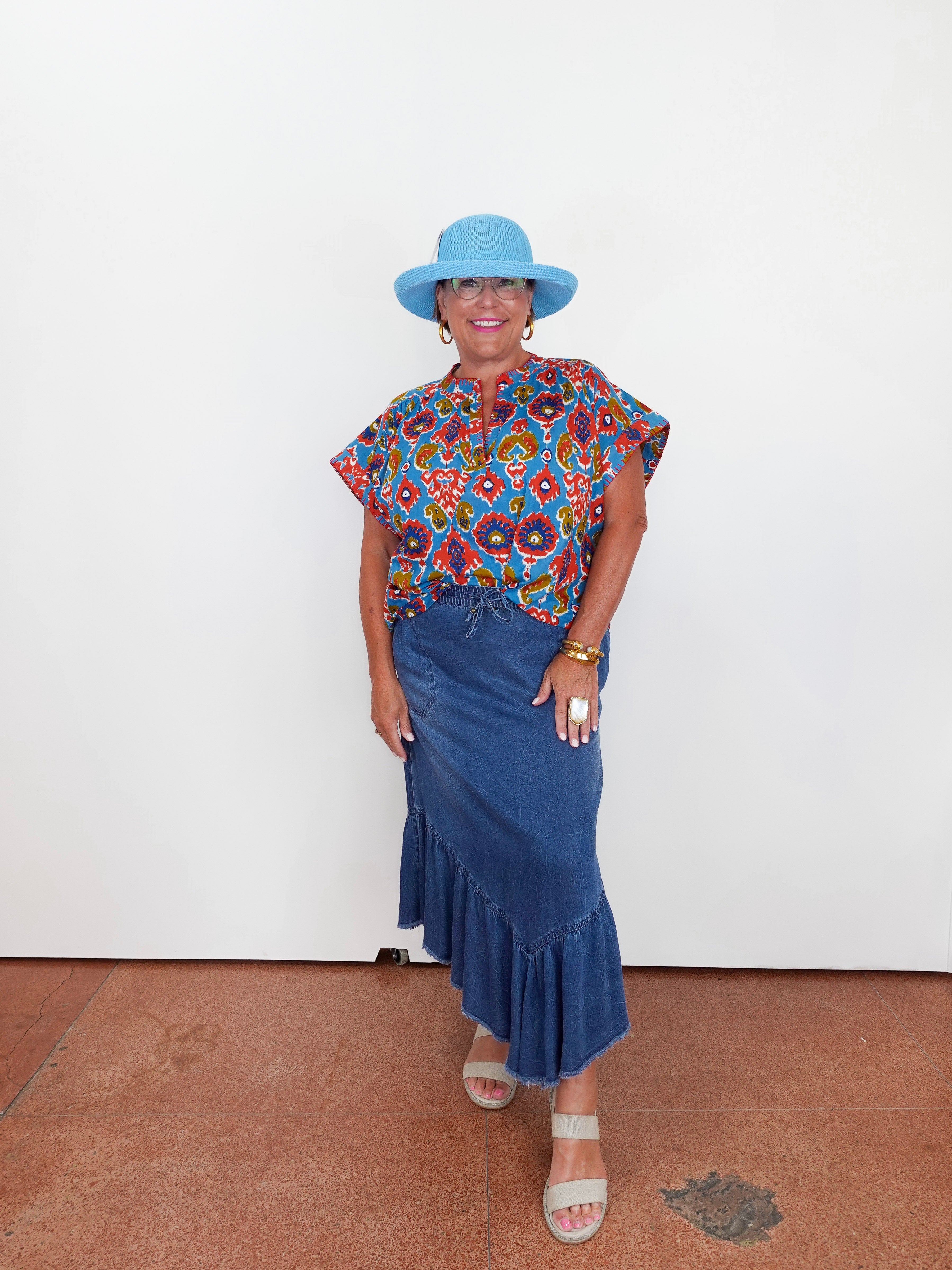 Woman wearing a colorful top and blue skirt with a blue hat against a white background