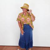 Woman wearing a patterned shirt, blue skirt, and straw hat on a plain background