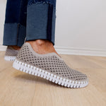 Person wearing gray slip-on shoes with white soles on a wooden floor.