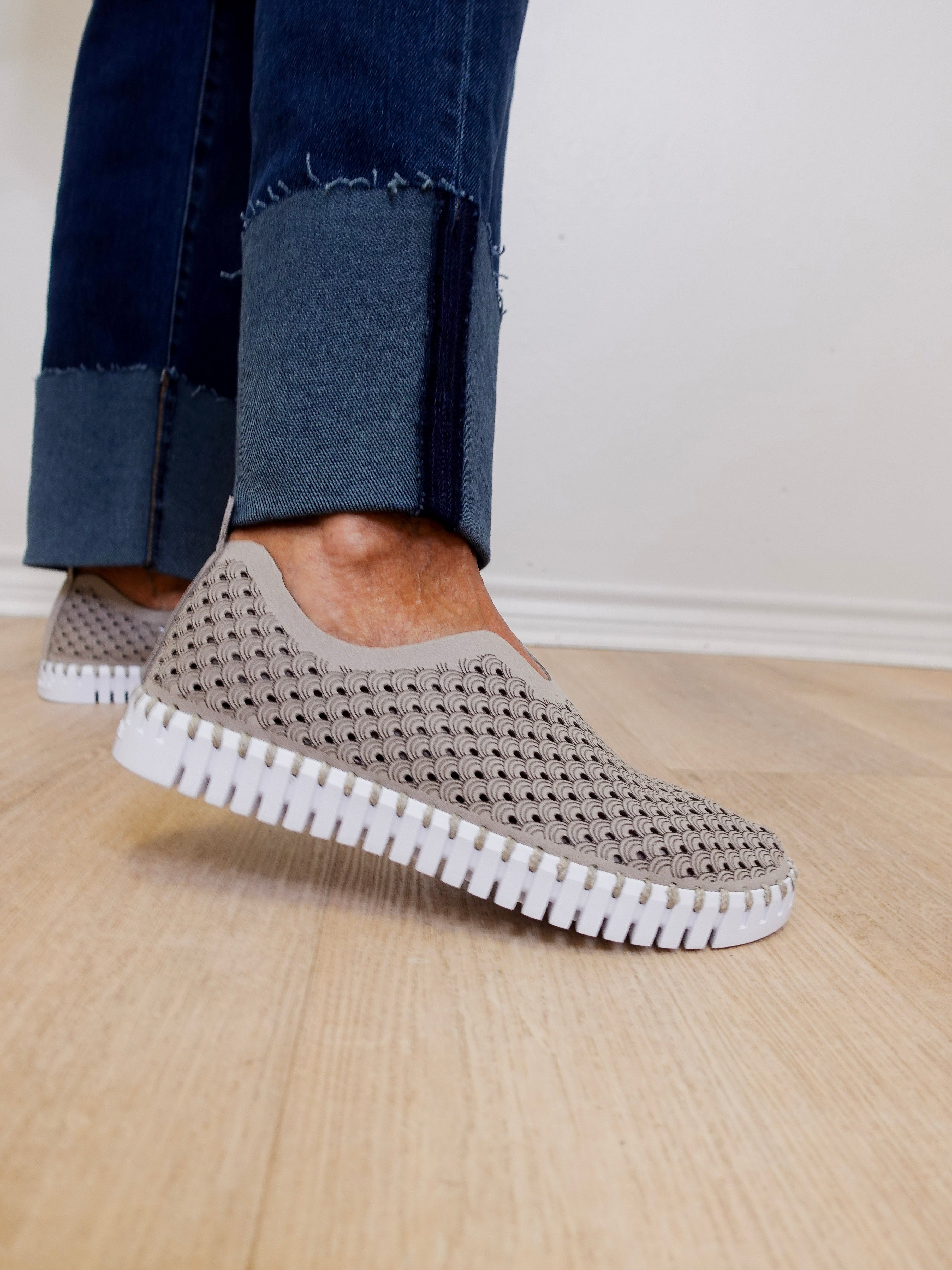 Person wearing gray slip-on shoes with white soles on a wooden floor.