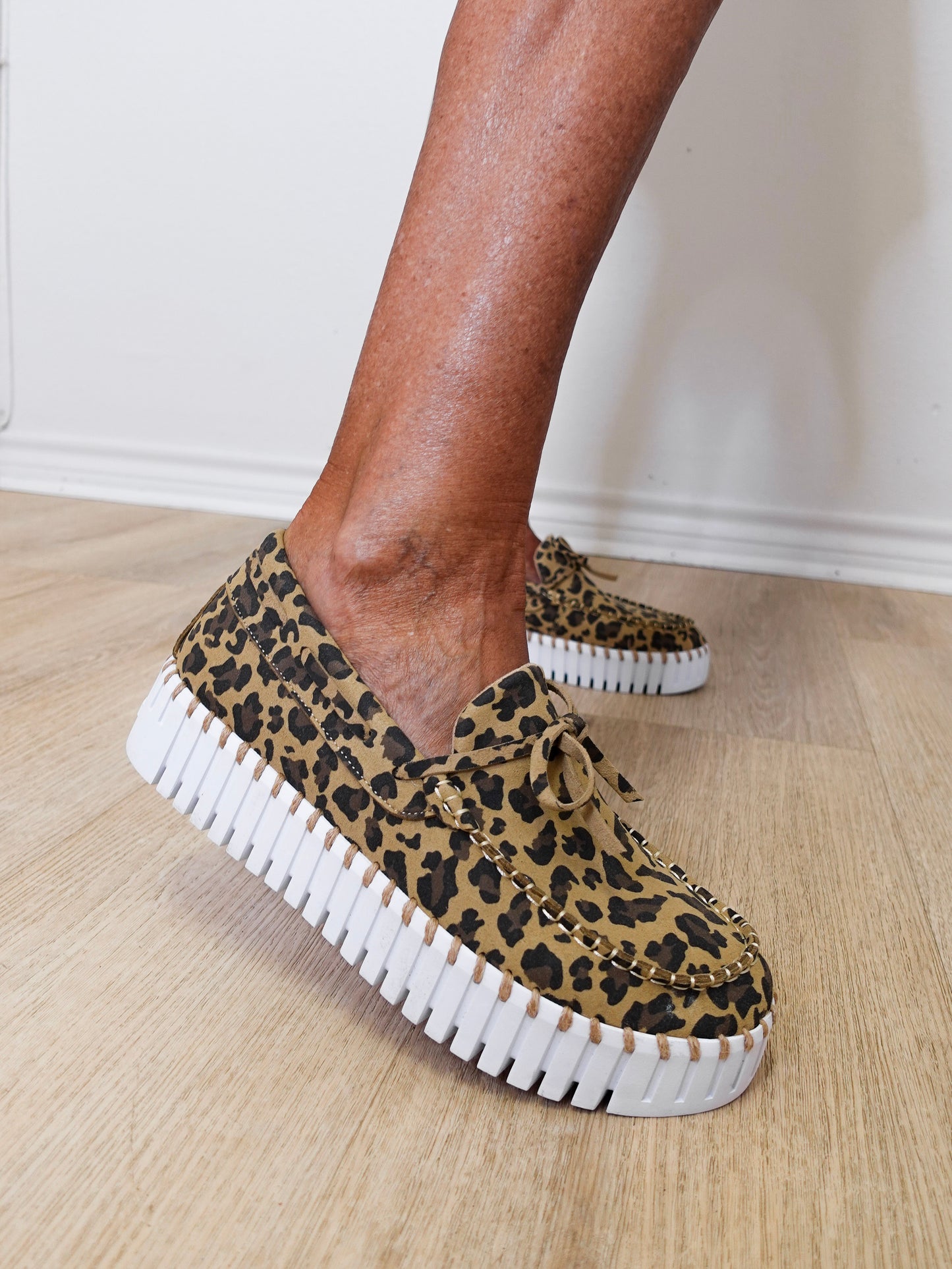 Leopard print sneakers with white soles worn by a person on a wooden floor.