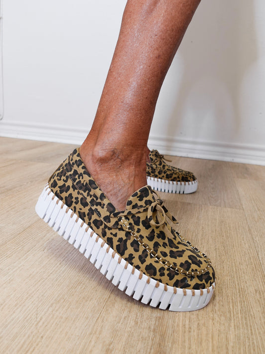Leopard print sneakers with white soles worn by a person on a wooden floor.