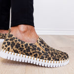 Leopard print slip-on sneakers with white sole worn indoors.
