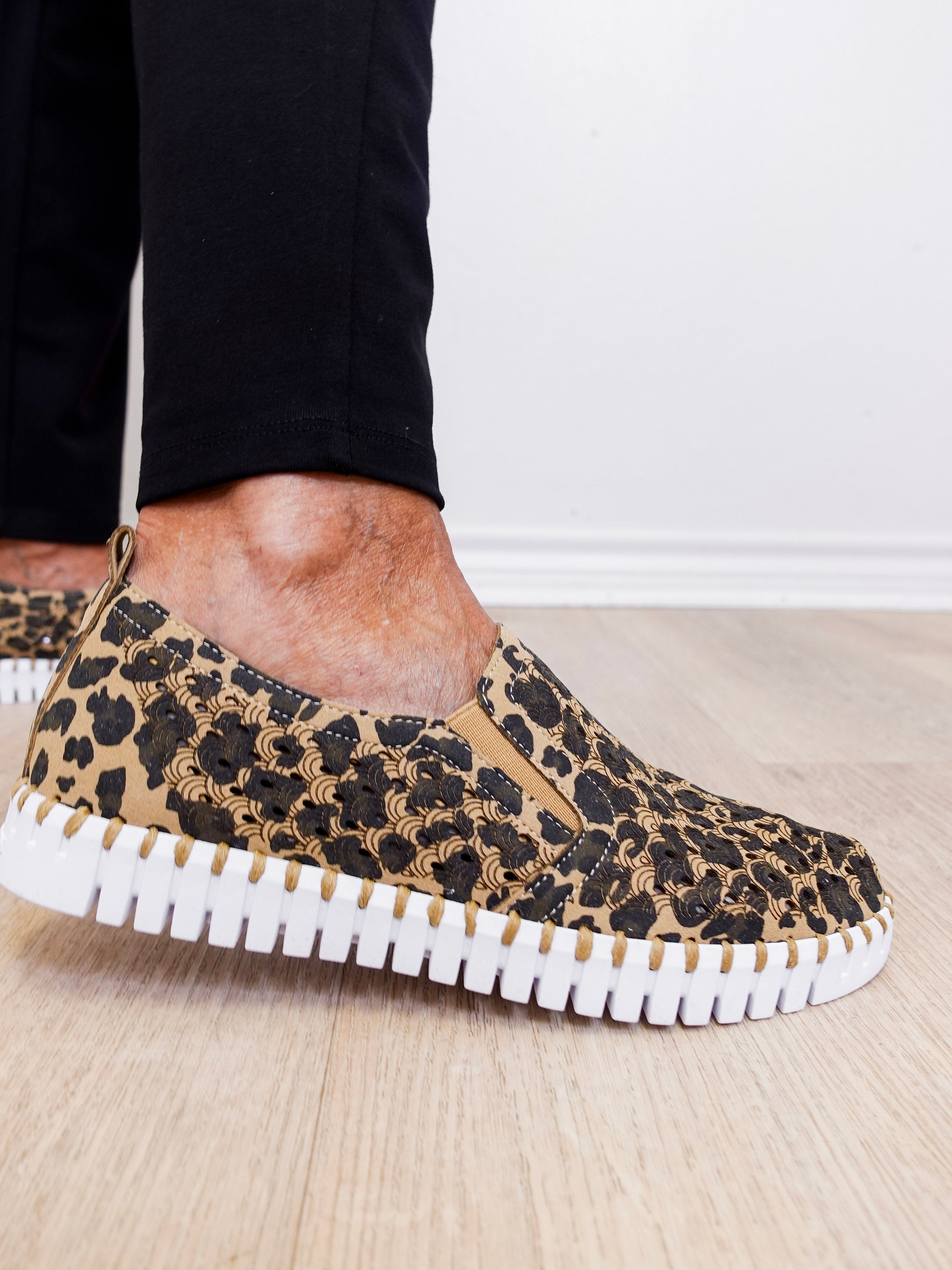 Leopard print slip-on sneakers with white sole worn indoors.