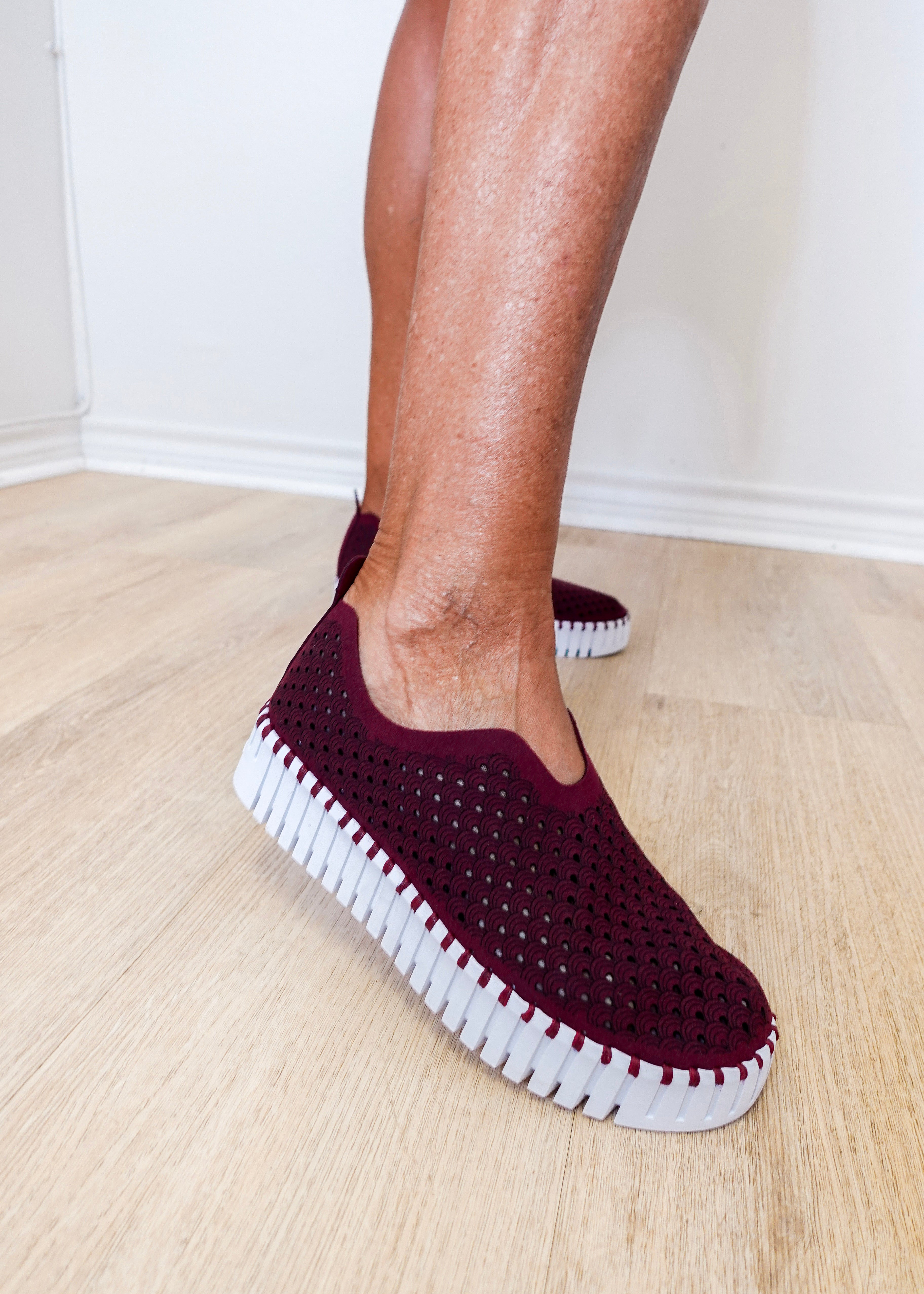 A woman wearing a maroon ilse Jacobsen flat against a white background. 