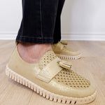 A person modeling a the ilse Jacobsen tassel loafer in gold against a white wall.
