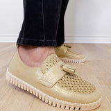 A person modeling a the ilse Jacobsen tassel loafer in gold against a white wall.