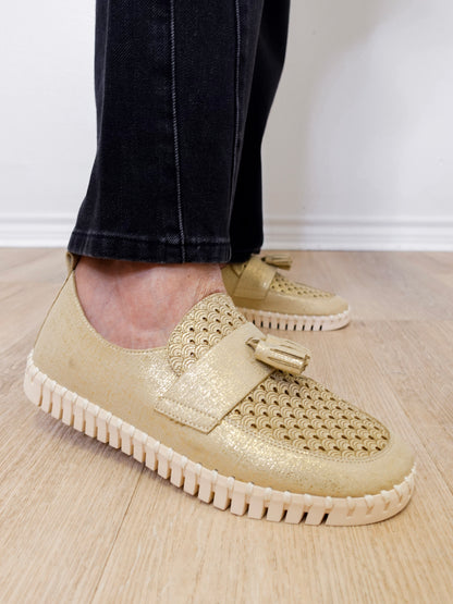 A person modeling a the ilse Jacobsen tassel loafer in gold against a white wall.