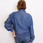 Person wearing a blue denim jacket and jeans against a white wall