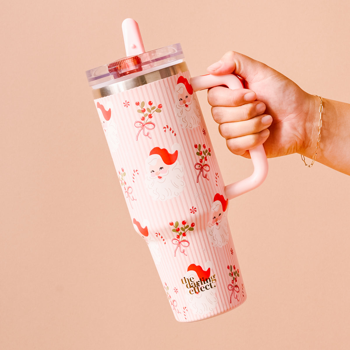 Hand holding a pink tumbler with a pattern and 'the walking' logo on a beige background