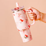 Hand holding a pink tumbler with a pattern and 'the walking' logo on a beige background