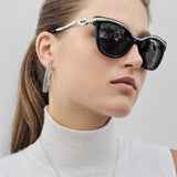Woman wearing black sunglasses and silver hoop earrings against a light background
