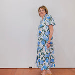 Woman wearing a floral dress standing against a plain white wall.