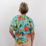Person wearing a colorful floral blouse with a plain background