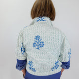 Person wearing a floral embroidered jacket with blue accents on a plain background