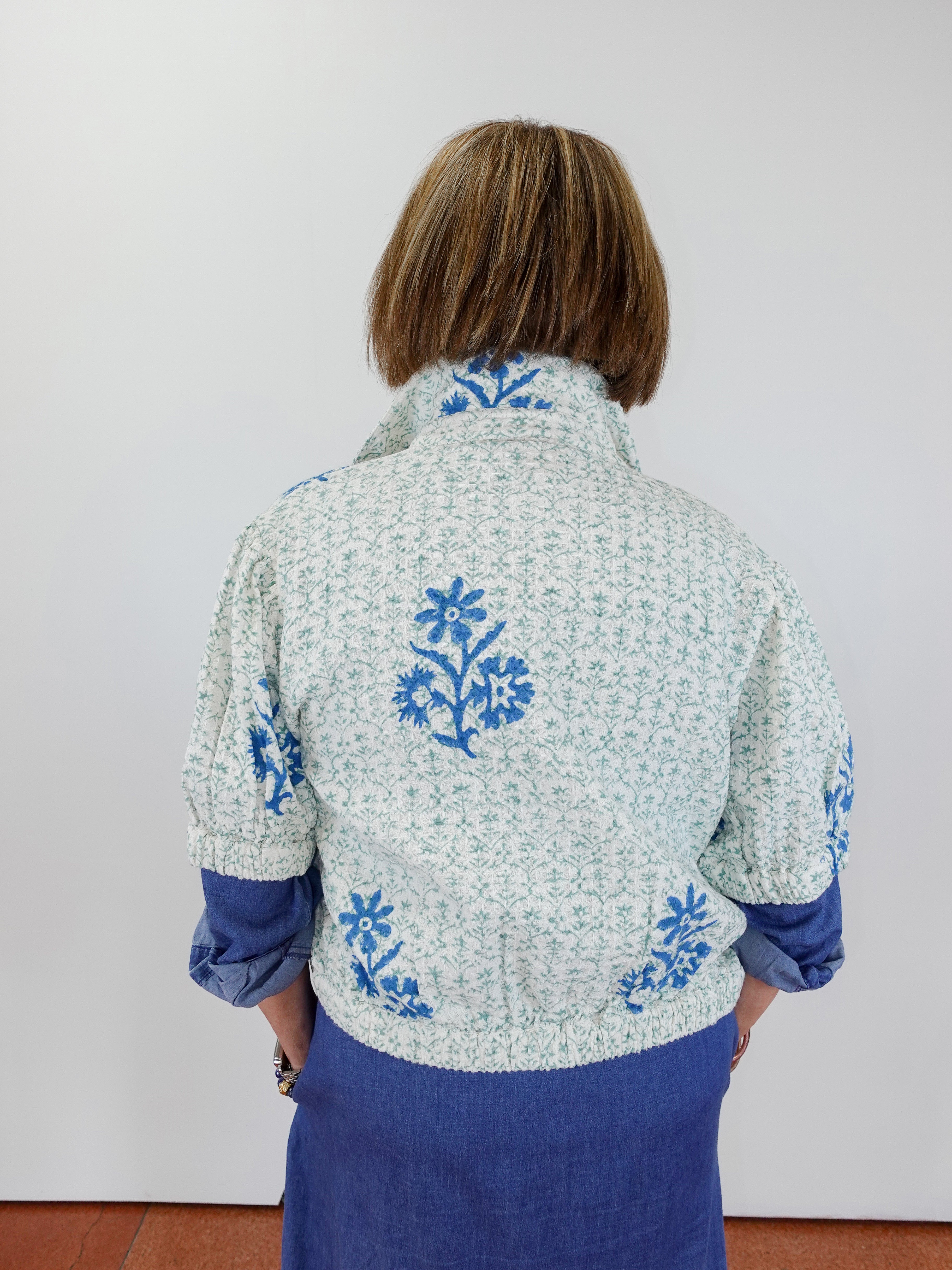 Person wearing a floral embroidered jacket with blue accents on a plain background