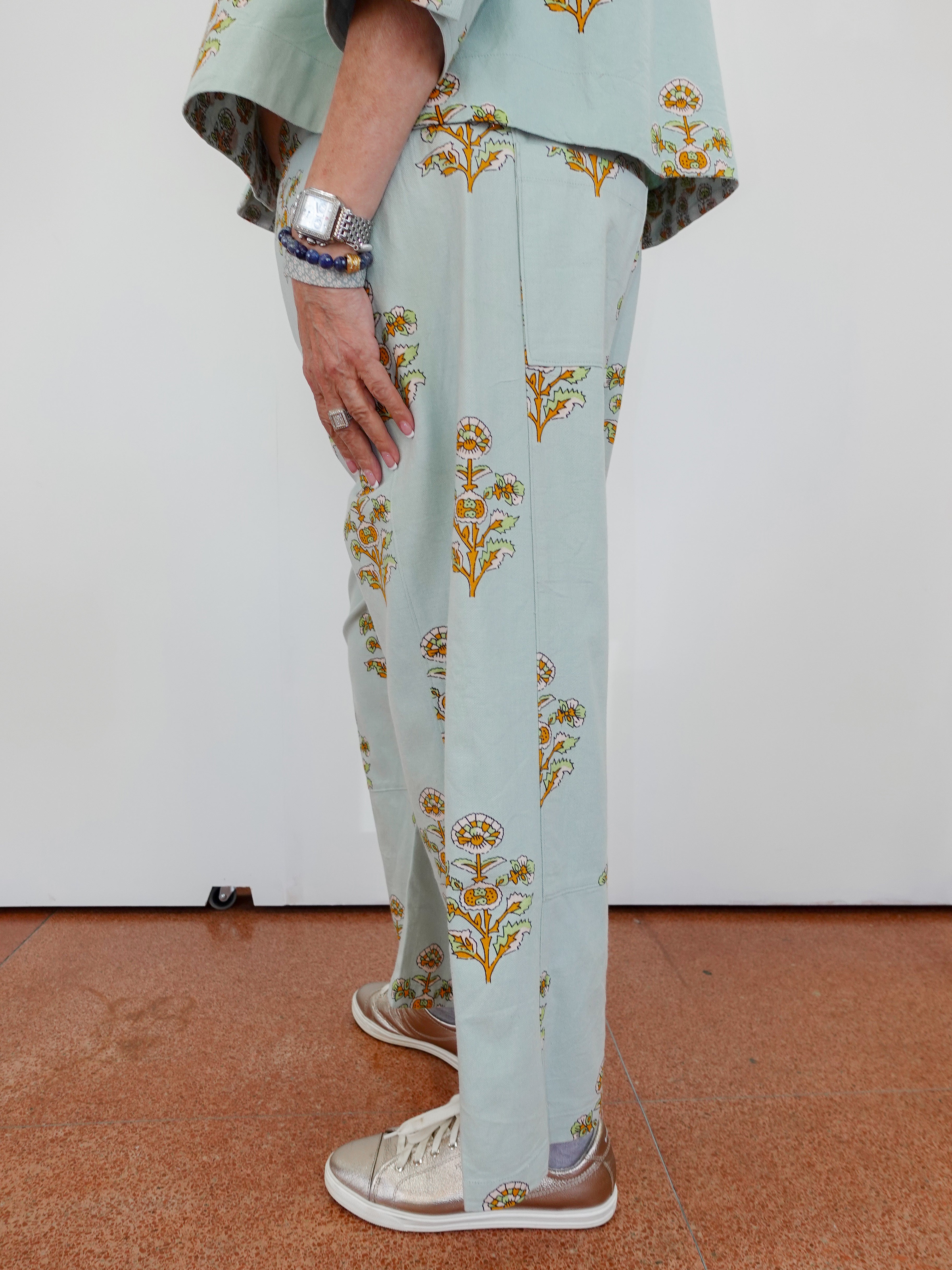 Light blue pants with gold floral patterns worn by a person on a white background