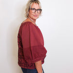 Woman wearing a burgundy blouse with a patterned overlay against a white background
