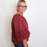 Woman wearing a burgundy blouse with a patterned overlay against a white background